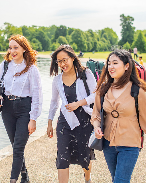 Three students walking in park past lake